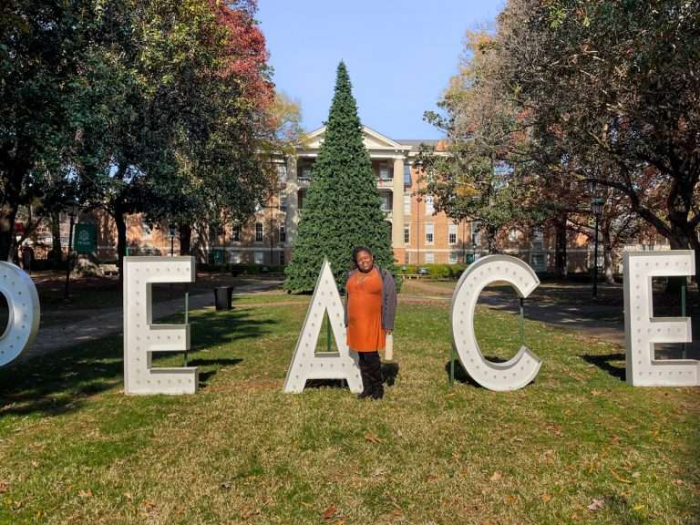 Chemae Mebane standing in front of large Peace letters, in front of William Peace University